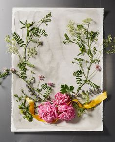 an arrangement of flowers and greenery on a piece of white paper with yellow ribbon