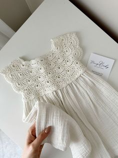 a hand holding a piece of cloth next to a white dress with crochet on it