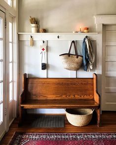 a wooden bench sitting under a window next to a basket and coat rack on a wall