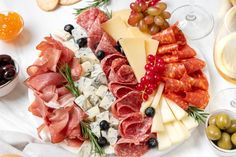 an assortment of cheeses, meats and olives are arranged on a platter