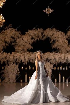 a woman in a white wedding dress standing on a stage with candles and flowers behind her