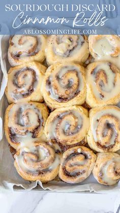 cinnamon rolls with icing in a white box on a marble counter top and text overlay that reads, sourdough disarrd cinnamon rolls