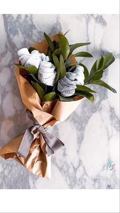 a bouquet of flowers wrapped in brown paper on a marble counter top with leaves and ribbons