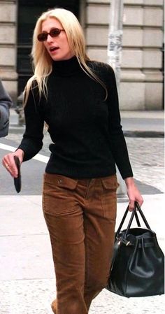 a woman walking down the street with a handbag in her other hand and wearing brown pants