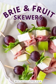 a plate with grapes, apples and prosciutto skewers on it