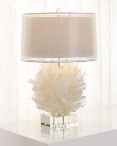 a white table lamp sitting on top of a desk next to a curtained window