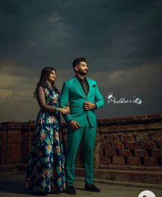 a man and woman standing next to each other in front of a dark cloudy sky