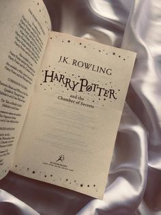 an open harry potter book sitting on top of a white satin covered bed sheet with the title'j k rowling, harry potter and the chamber of secrets '