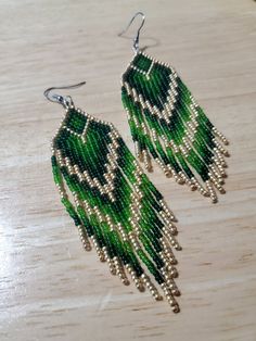 green and silver beaded earrings sitting on top of a wooden table