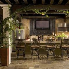 an outdoor kitchen and dining area with potted plants on the counter, television mounted to the wall