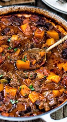 a pot full of stew with a spoon in it and two plates on the side