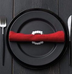 a black plate topped with a red napkin and silverware next to utensils