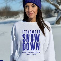 a woman wearing a white snow down sweater and blue beanie standing in the snow