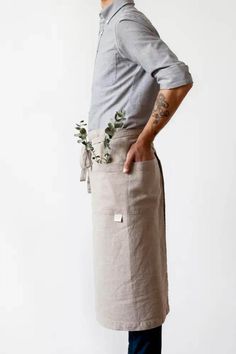 a man wearing an apron with flowers in his pocket, standing against a white background