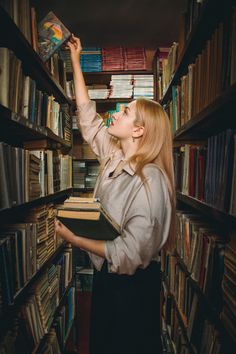 a woman is reaching for books in a bookcase and looking up at the sky