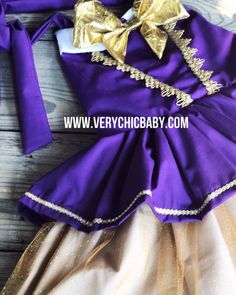 a purple dress with gold trims and a bow on the back is laying on a wooden surface