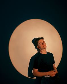 a man is standing in front of a large white circle with his eyes closed and one hand on his chest