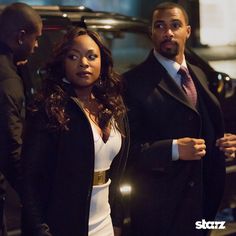 a man and woman standing next to each other in front of a car at night