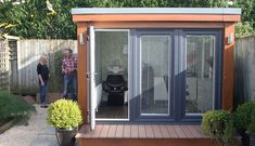 two men are standing next to a small garden shed with sliding doors on the outside