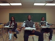 three people sitting at desks in front of a chalkboard