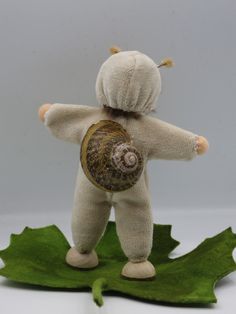 a stuffed animal with a snail on it's back sitting on a green leaf