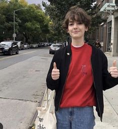 a young man is giving the thumbs up sign in front of his bag on the sidewalk