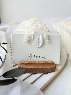 a close up of a wooden block on a table with white flowers and greenery