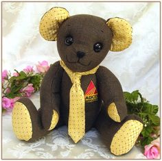 a brown teddy bear wearing a yellow tie and sitting on a white surface with pink flowers in the background