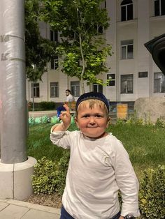 a young boy standing next to a pole on the sidewalk with his hands in the air