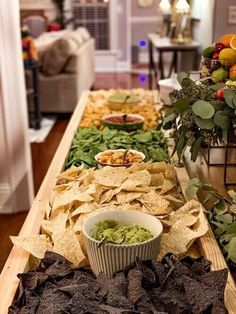 an assortment of food is displayed on a long table with chips and salsa in bowls