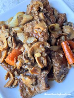 a white plate topped with meat and veggies next to carrots on a table