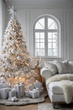 a white christmas tree with presents under it in front of a couch and large window