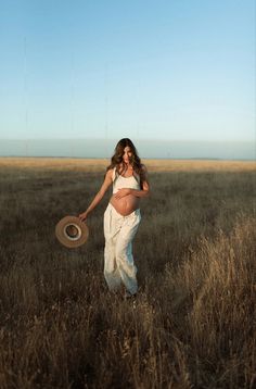 a pregnant woman standing in a field holding a frisbee