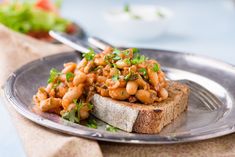 a piece of bread with beans on it sitting on a plate next to a salad