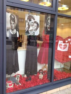 a window display with red roses and pictures in it's glass front windows, including two mannequins