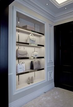 a display case filled with purses and handbags in a white walled room next to a black door