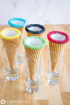 four ice cream cones with colored sprinkles in them on a wooden table