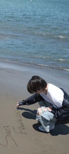 a young boy writing in the sand at the beach