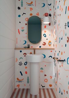 a bathroom with colorful wallpaper and a white pedestal sink in the corner next to a mirror