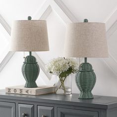 two green vases sitting on top of a table next to a book and lamp