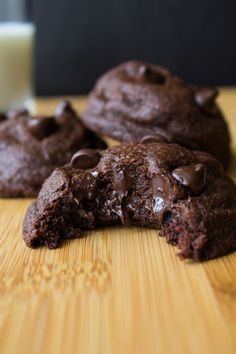 three chocolate cookies on a cutting board with a glass of milk in the background and one half eaten