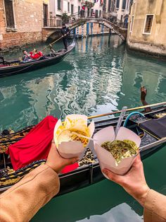 two people holding food in their hands while on a gondola ride down the canal