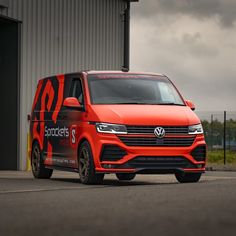 an orange vw transport van parked in front of a building with dark clouds overhead