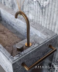 a bathroom sink with gold faucet and marble counter top in front of columns