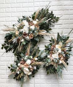 two wreaths with flowers and greenery hanging on a brick wall in front of a white brick wall