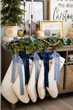 christmas stockings hanging from a mantle with blue bows and greenery on them in front of a fireplace