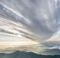 the sky is filled with clouds and mountains in the distance are foggy, low lying hills