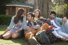 a group of people sitting next to each other on the grass near a tree and building