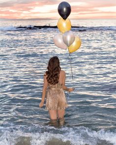 a woman standing in the ocean holding balloons