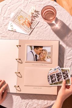 a person holding an open photo album on top of a table with pictures and glasses